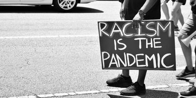 Person holding a sign saying 'Racism is the pandemic' at a protest.