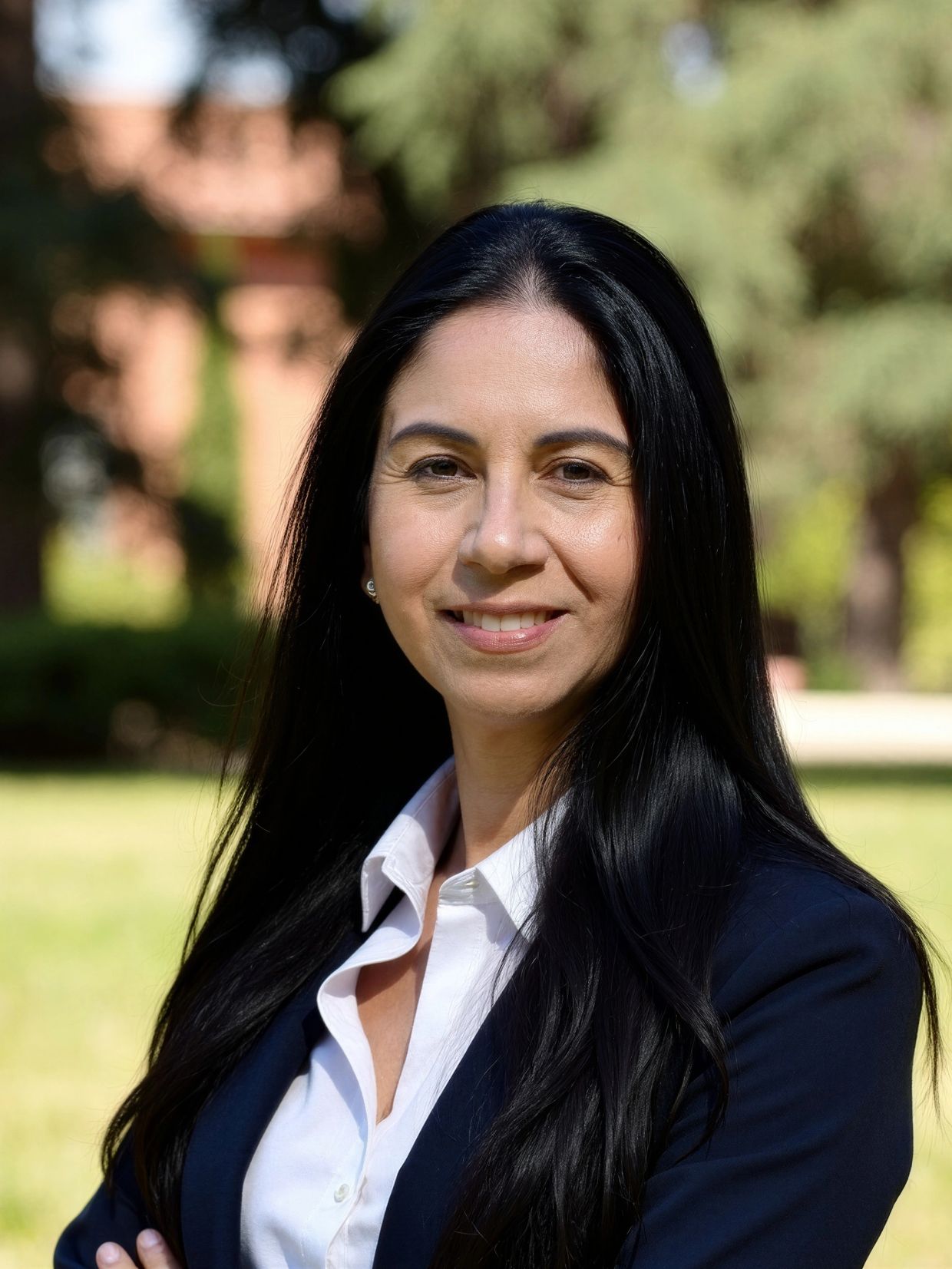 Professional woman with long black hair smiling outdoors in business attire.