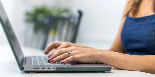 Woman with manicured nails typing on a laptop keyboard.