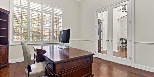 Elegant home office with wooden desk, leather chair, and large windows.