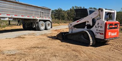 Bobcat excavator and a trailer on a dirt construction site under a clear blue sky.