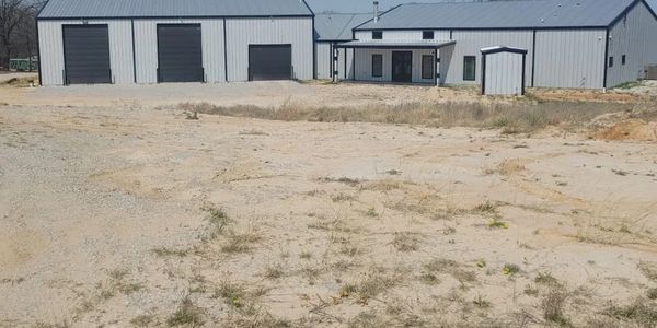 Large metal warehouse building with multiple garage doors on a dry, grassy plot.