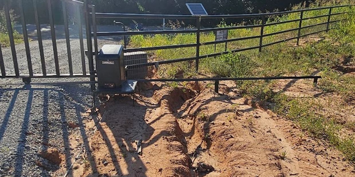Tire tracks in dry soil leading to a closed gate on a sunny day.