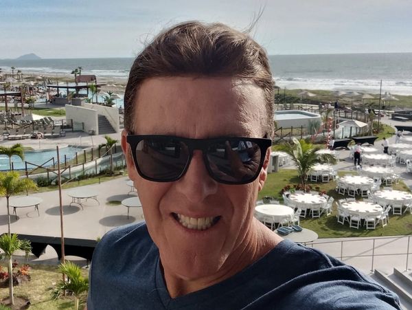 Man wearing sunglasses with a beach and event setup in the background.