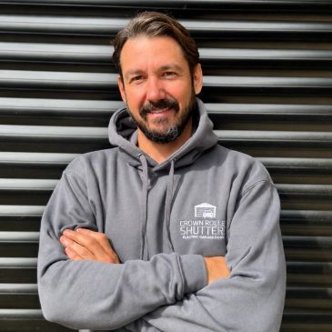 Man smiling with arms crossed in a gray hoodie.