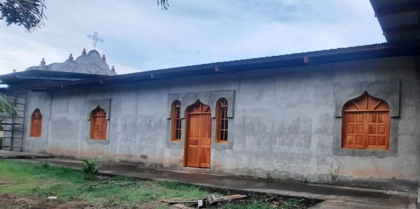 A simple concrete church building with wooden doors and windows under a cloudy sky.