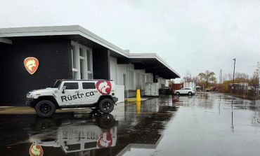 A Rustr.ca branded white SUV parked outside a warehouse on a rainy day.