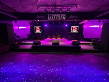 Empty stage with purple lighting and screens at Rüstr venue.