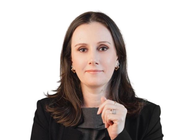 Mulher sorridente com blazer preto e fundo branco.