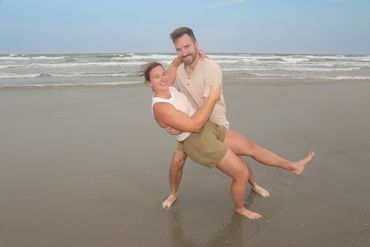 A couple joyfully posing on a beach with waves in the background.