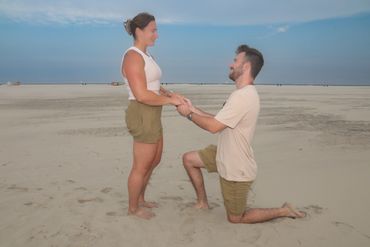 A man proposes to a woman on a sandy beach at sunset.