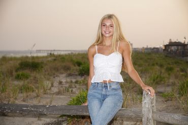Young woman smiling by a beach fence at sunset.