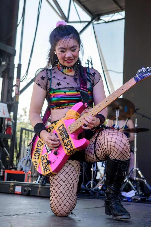 Female guitarist in colorful outfit playing a pink guitar on stage.