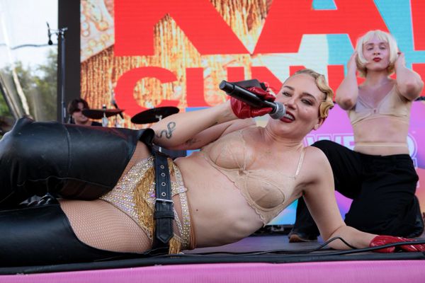 Performer in fishnet tights and leather boots sings on stage with backup dancer.