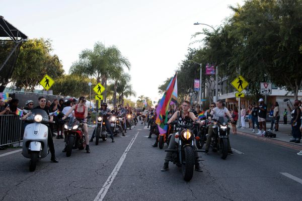 Motorcyclists with pride flags participating in a parade on a city street.