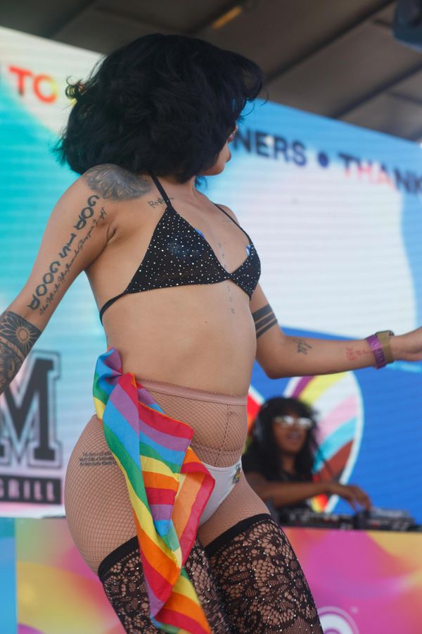 A tattooed performer in fishnet stockings and a rainbow flag dances on stage.