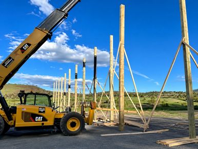 A CAT forklift lifting wooden posts for a structure under construction outdoors.