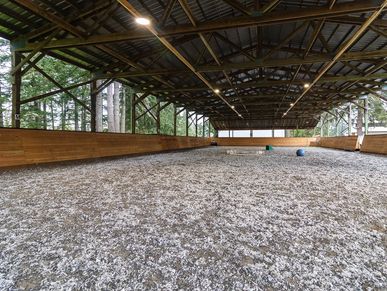 Covered equestrian arena with wood paneling and gravel floor.