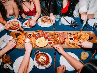Friends sharing a large brunch platter with waffles and fried chicken.