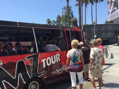 People boarding a red MTZ Tour bus on a sunny day.