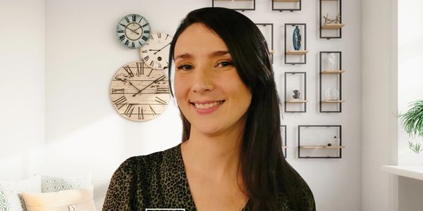 A smiling woman with long dark hair in a cozy, stylish living room.