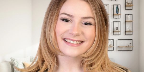 A young woman with blonde hair smiling warmly indoors.