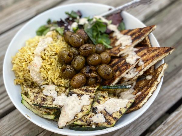 Grilled vegetable and pita bowl with rice, olives, greens, and creamy dressing.