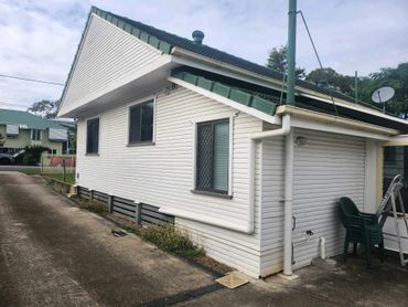 Small white house with green roof and driveway beside it.