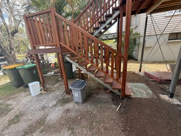 Wooden outdoor staircase with trash bins underneath.