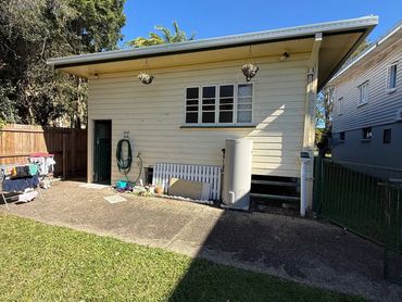 Small backyard shed with gardening tools and a water tank.
