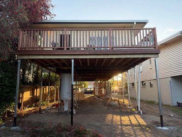 Elevated wooden deck with metal supports in a backyard at sunset.