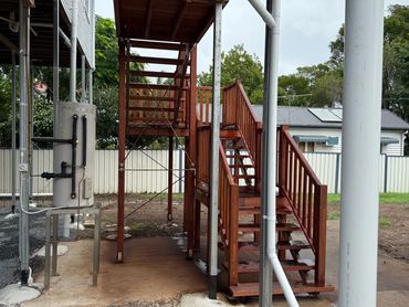 Wooden outdoor staircase with metal railing under a shelter frame.