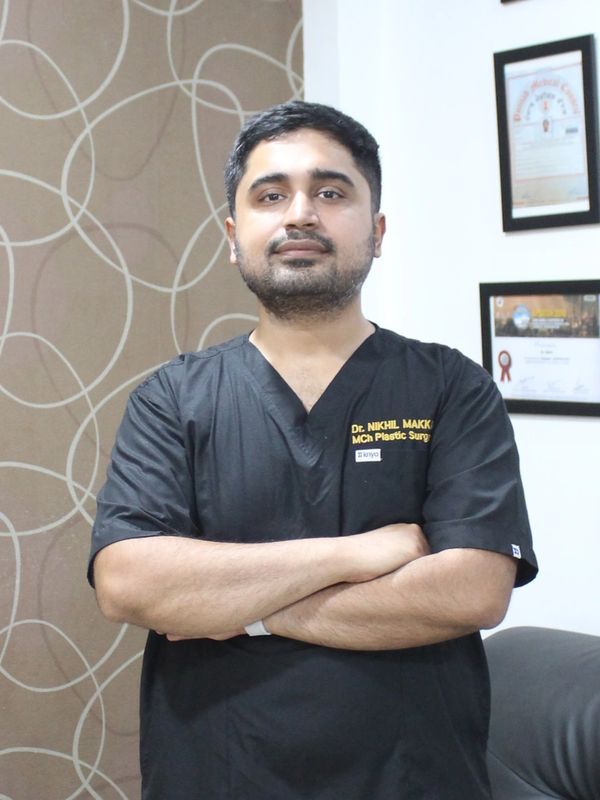 Doctor in black scrubs standing confidently with arms crossed in an office.