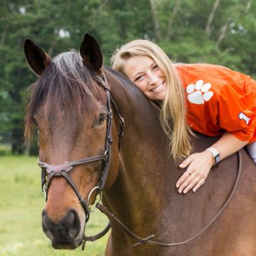 A smiling woman hugging a brown horse outdoors.