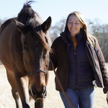 A woman walking happily alongside a brown horse outdoors.