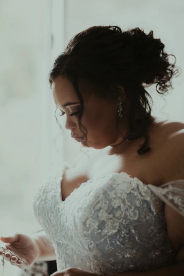 a beautiful bride admires her jewelry, as her mother buttons her dress off camera. 