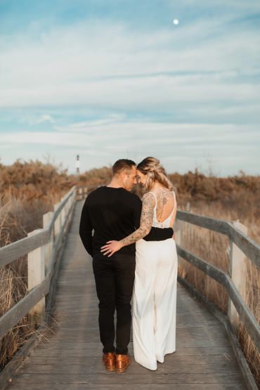 Just married couple embrace under a full moon on a boardwalk to the Fire Island lighthouse.