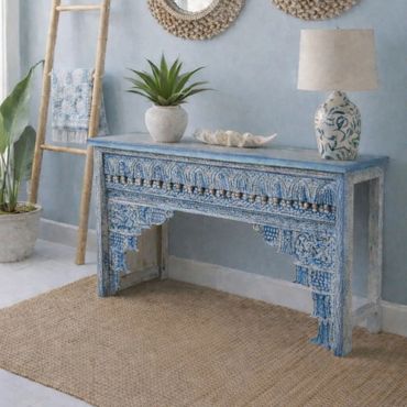 Blue carved wooden console table with decor against a light blue wall.