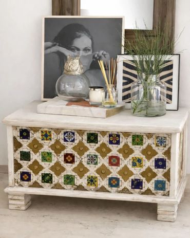 Decorative chest with colorful tiles and framed art on top.