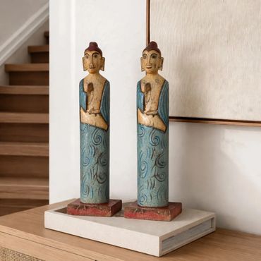 Two tall, carved wooden statues with blue robes and red bases on a table.