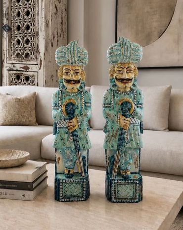 Two intricately designed blue-green warrior statues on a marble table.
