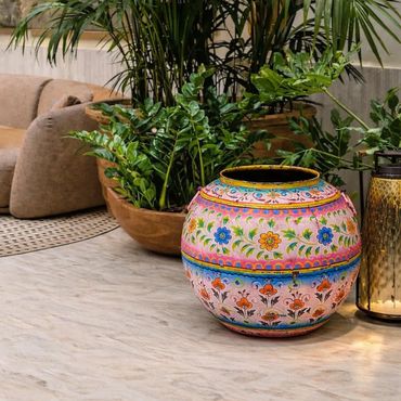 Colorful floral ceramic pot on a marble surface with green plants and cozy sofa in the background.