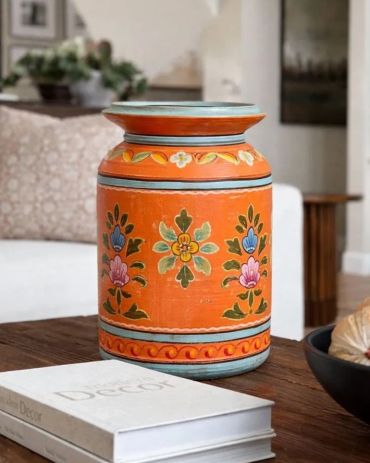 Colorful orange decorative vase with floral patterns on a wooden table.