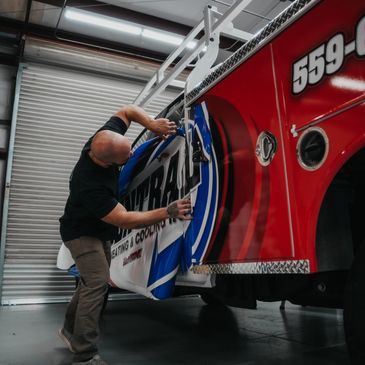 Man applying a large decal to a red truck inside a garage.