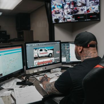 Man with tattoos working on computer with multiple screens and surveillance footage.