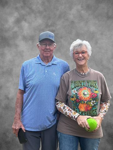 Elderly couple smiling, posing with a green ball against a gray background.
