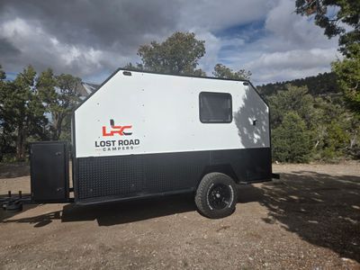 Compact Lost Road camper trailer parked in a forest clearing.