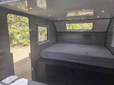 Cozy camper interior with a bed and multiple windows overlooking greenery.