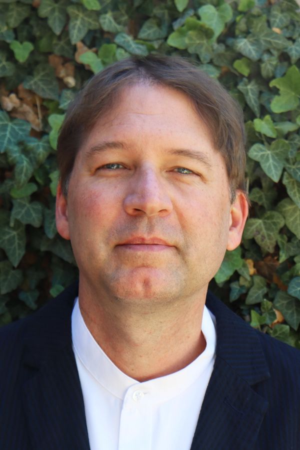 Portrait of a man in a suit with a leafy background.