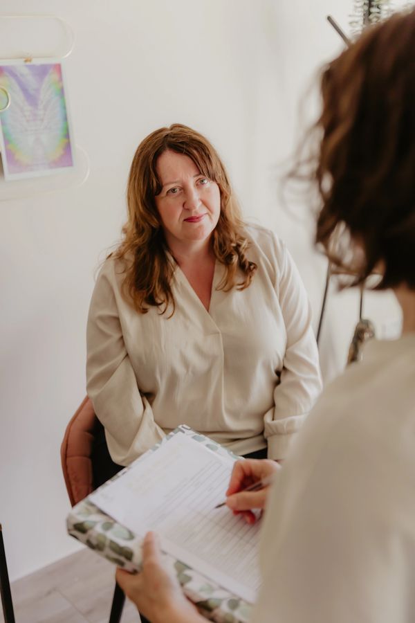 Woman in a beige blouse talking to another person with a clipboard.